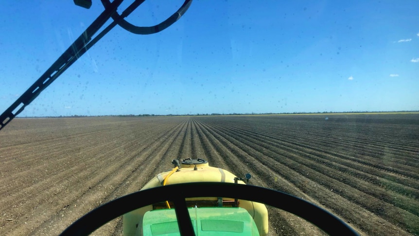 Looking from inside a tractor cab, over the steering wheel and out onto a neatly ploughed paddock. The sky is blue and cloudless