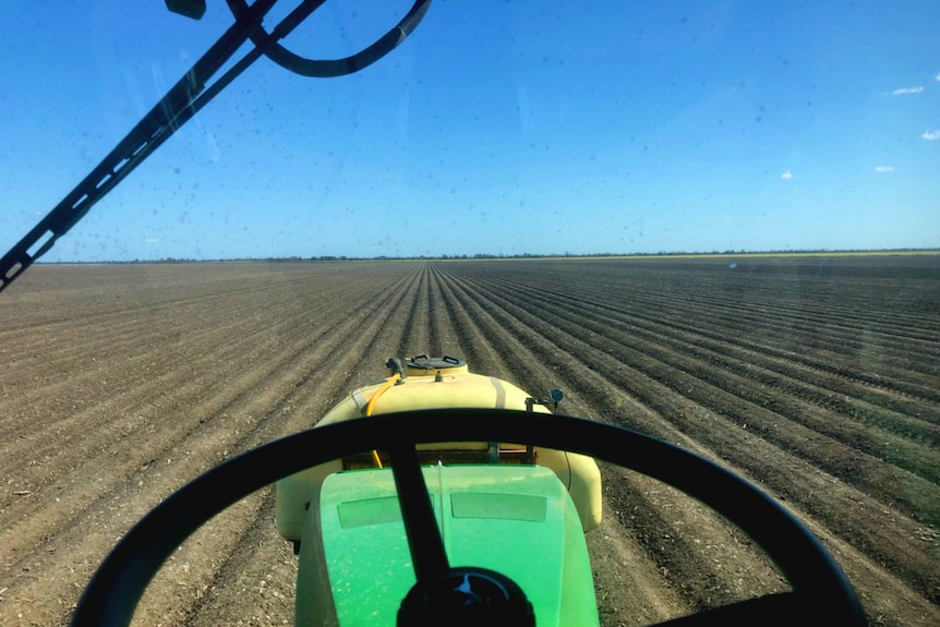 Looking from inside a tractor cab, over the steering wheel and out onto a neatly ploughed paddock. The sky is blue and cloudless