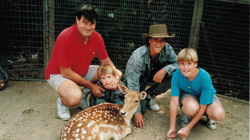 Medium portrait shot of a man and three children crouched down in an enclosure next to a deer.