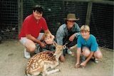 Medium portrait shot of a man and three children crouched down in an enclosure next to a deer.