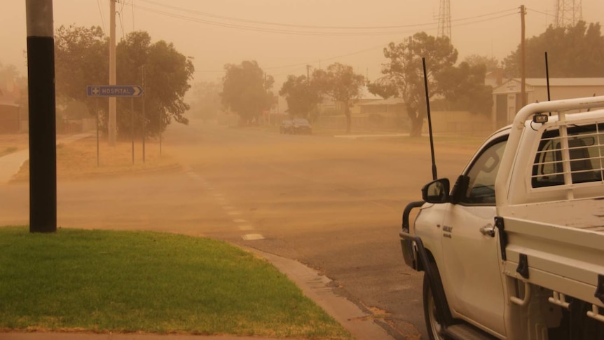 A ute on a road surrounded by dust.