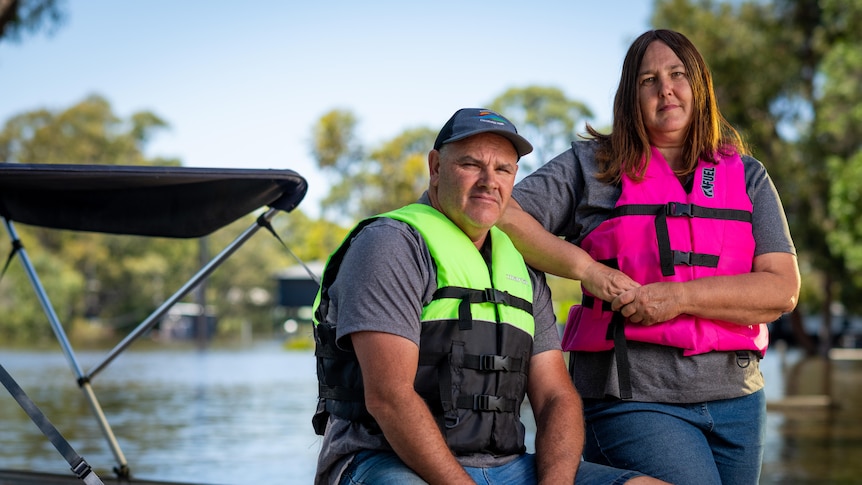A man and a woman wearing lifejackets next to a boat