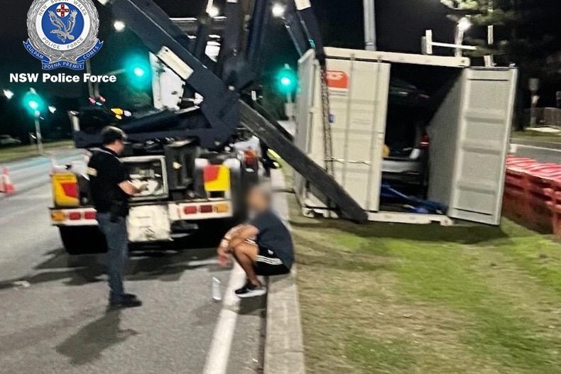 cops pull over a truck with a container, a man sits on the gutter