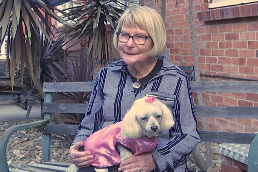 Dawn Crichlow sits on garden chair with her dog, Princess Pookie dressed in cape and bow on her lap