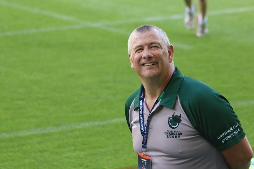 Neil Hay stands on a football field in a Melbourne Chargers jersey smiling at the camera