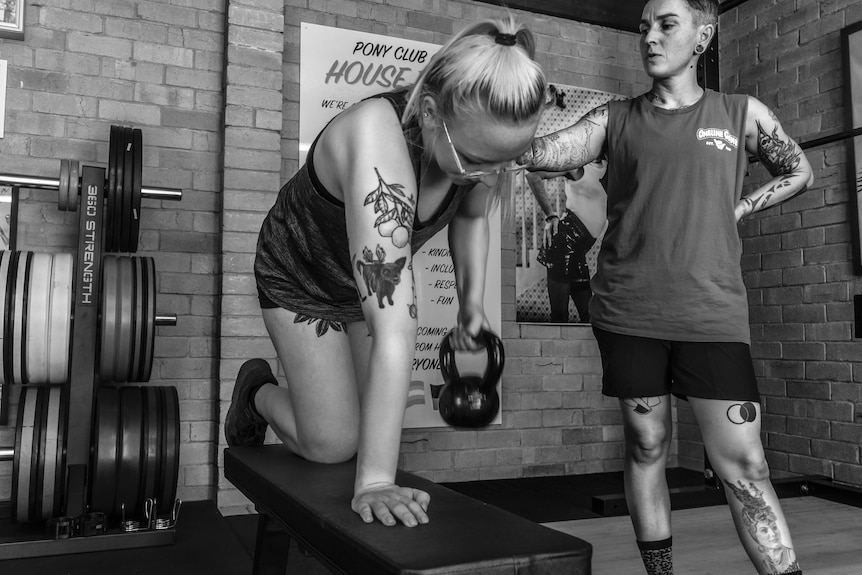 Ella Mason stands next to a client while they do weights.