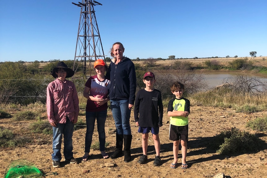 Mother and four kids standing in front of outback dam with windmill behind them