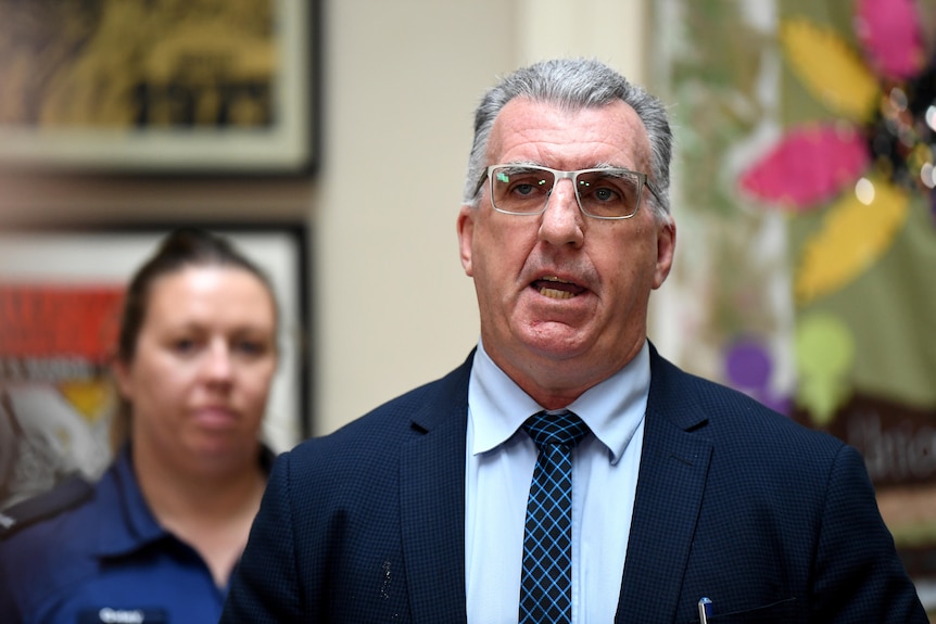 A man with glasses standing in front of a health worker. 