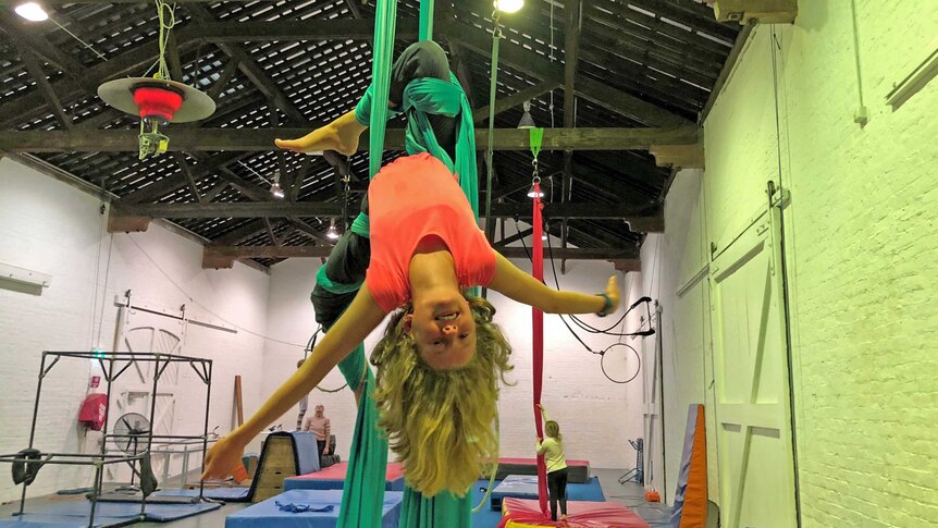 Harriet O'Shea Carre hangs upside down with green fabric wrapped around her legs.