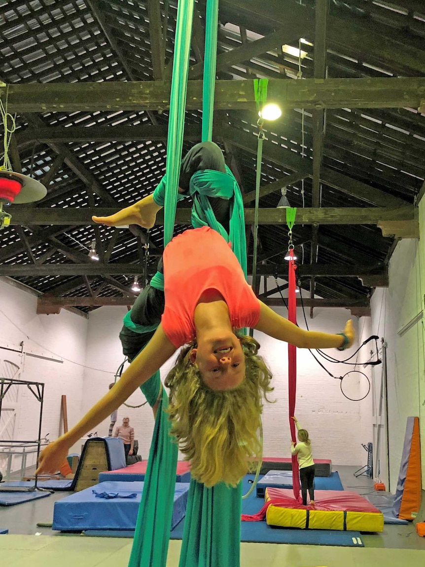 Harriet O'Shea Carre hangs upside down with green fabric wrapped around her legs.