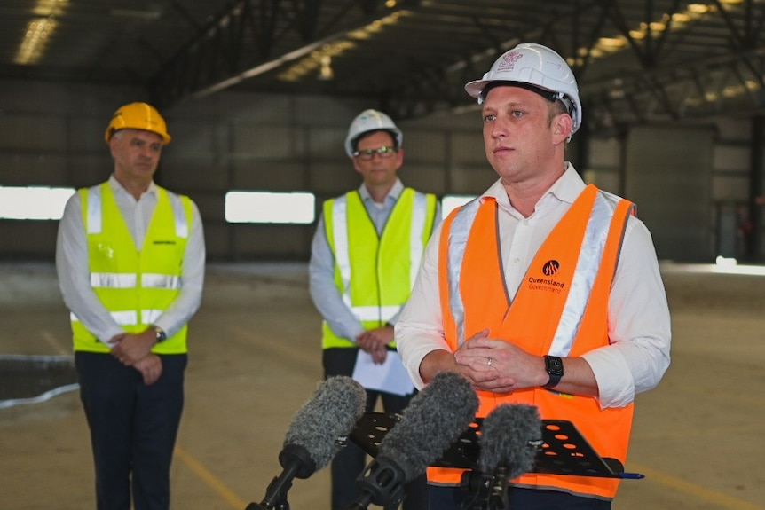 Deputy Premier Steven Miles in high vis and hard hat in front of a microphone.