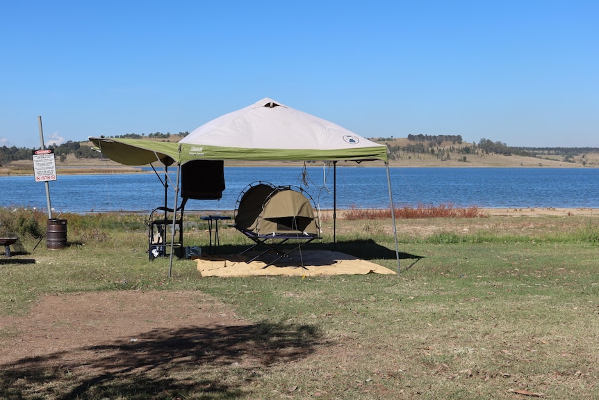 A camping gazebo set up beside a large lake on a sunny day.