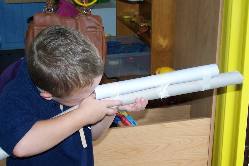 top of boy's head as he looks into a gun barrel made of paper/cardboard