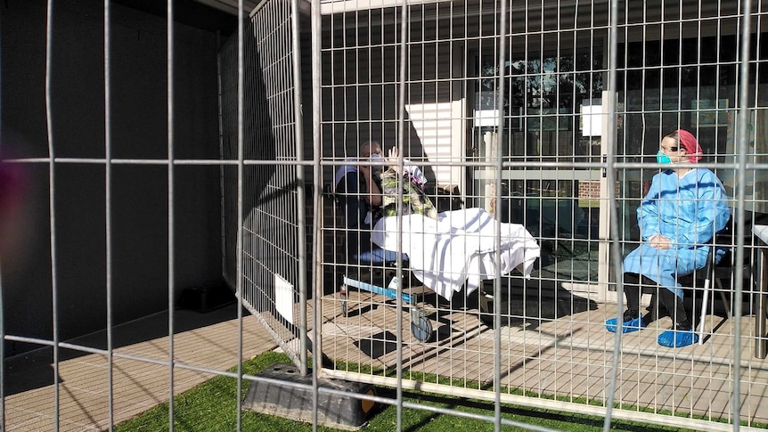 Two women in masks behind a metal fence aged care facility.