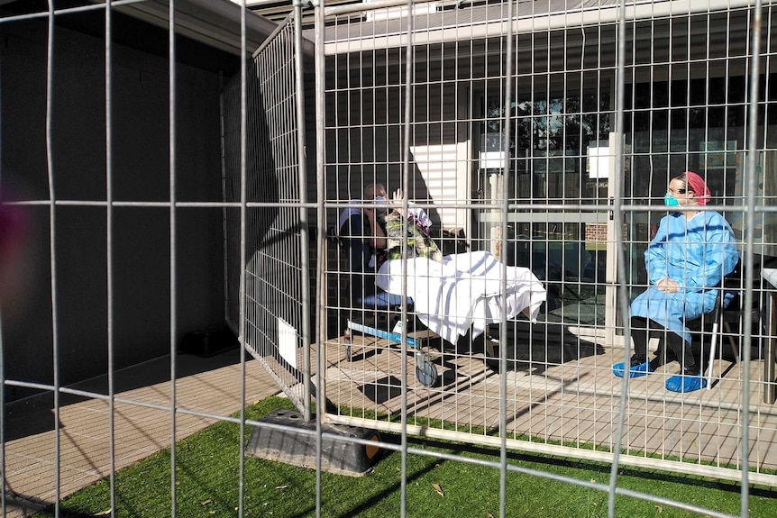 Two women in masks behind a metal fence aged care facility.