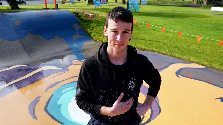 Kitt Bennett poses for a photo on the Millicent skatepark mural he has just painted of a giant purple and orange squid.