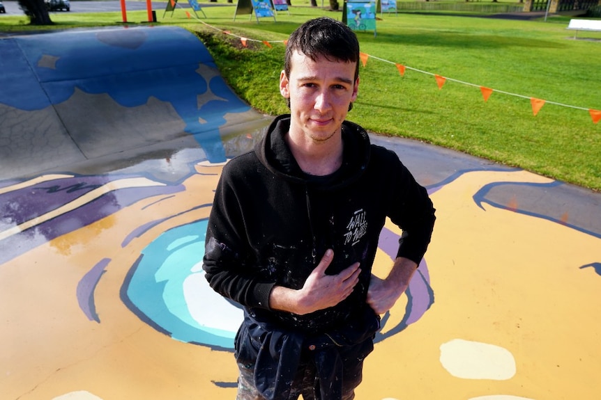 Kitt Bennett poses for a photo on the Millicent skatepark mural he has just painted of a giant purple and orange squid.