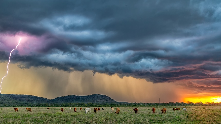 Clouds with a snippet of red sky lightning striking out onto pasture and a small hill behind