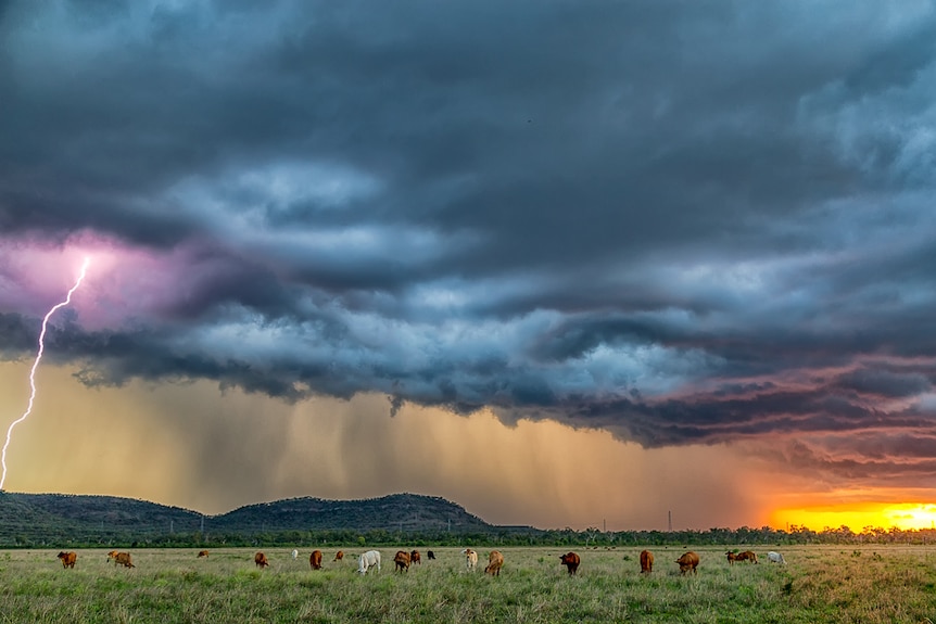 Clouds with a snippet of red sky lightning striking out onto pasture and a small hill behind