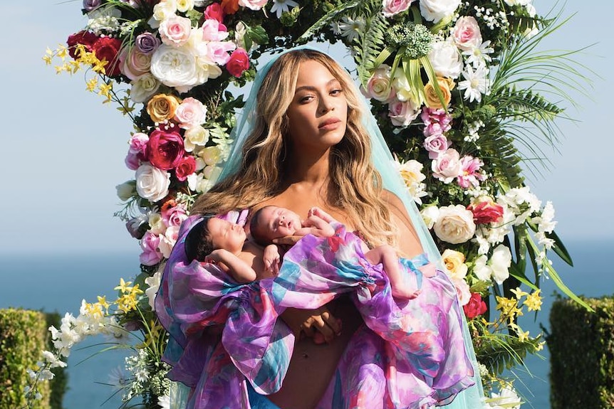 Singer Beyoncé with her one-month-old twins Rumi and Sir, wearing veil, with flowers behind her.