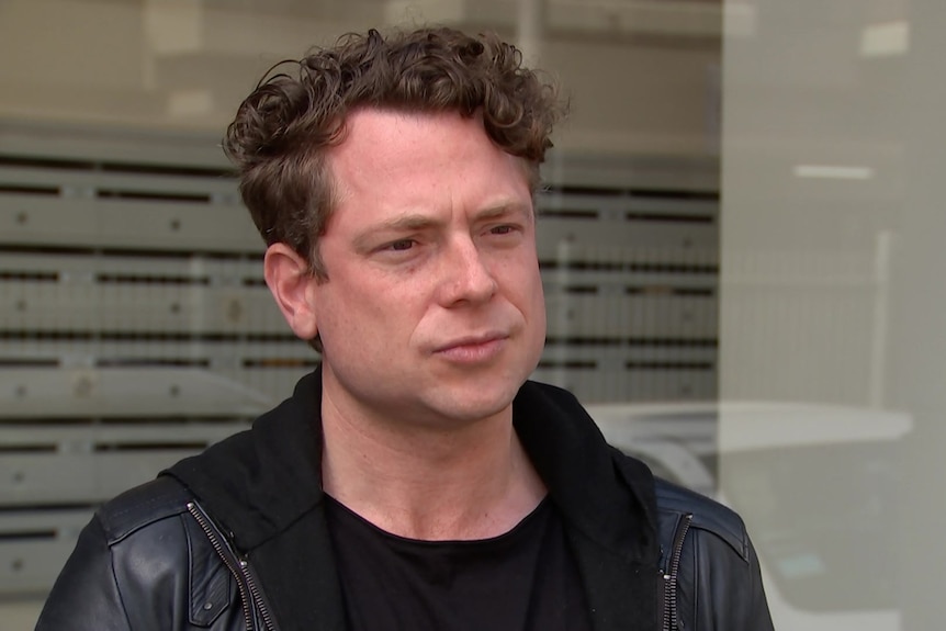 A man in a leather jacket in front of a window