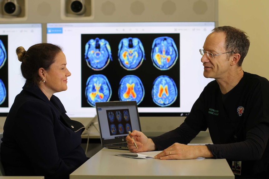 patient, Cindy black sitting with doctor talking through test results with brain scans in background