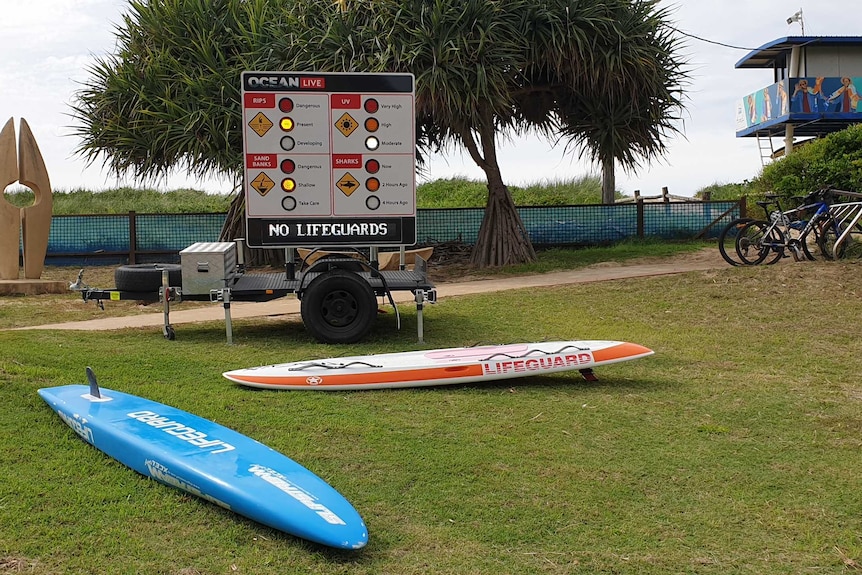 Surf boards lie on grass in front of a beach safety sign