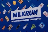 A billboard with common grocery items on a blue background surrounding the word "MILKRUN".