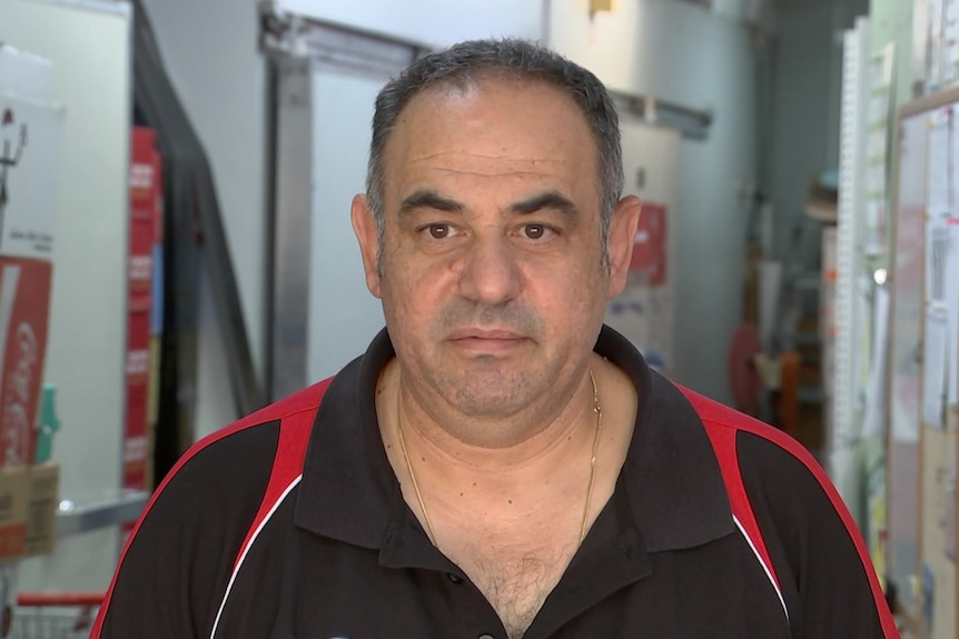 A man in a black and red polo shirt looks at the camera.