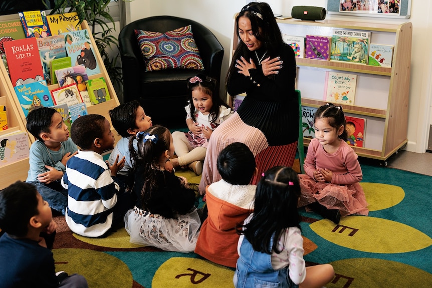 A small group of young children sitting together in front of a playgroup leader.