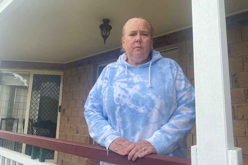 A woman in a tie dye jumper stands on her verandah