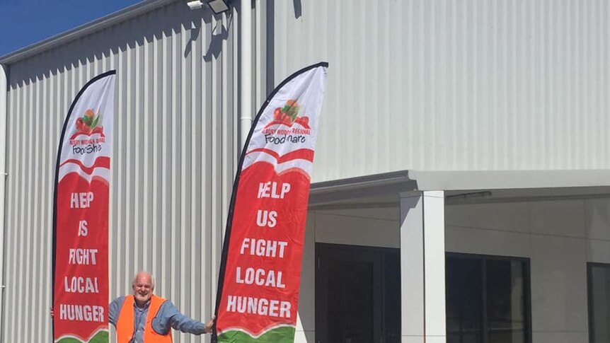 A man stands outside of a building between two red flags.