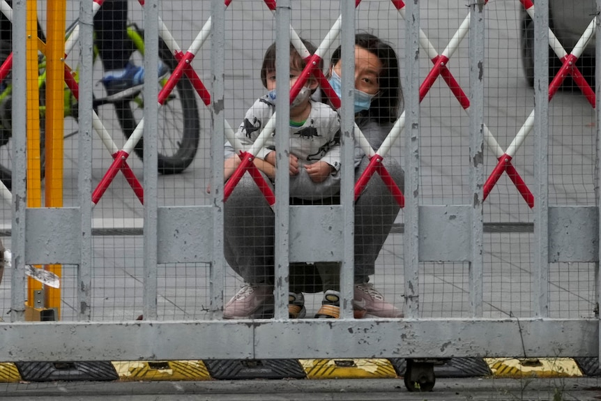 一个蹲着的女人带着一个小孩，透过栅栏往外看。