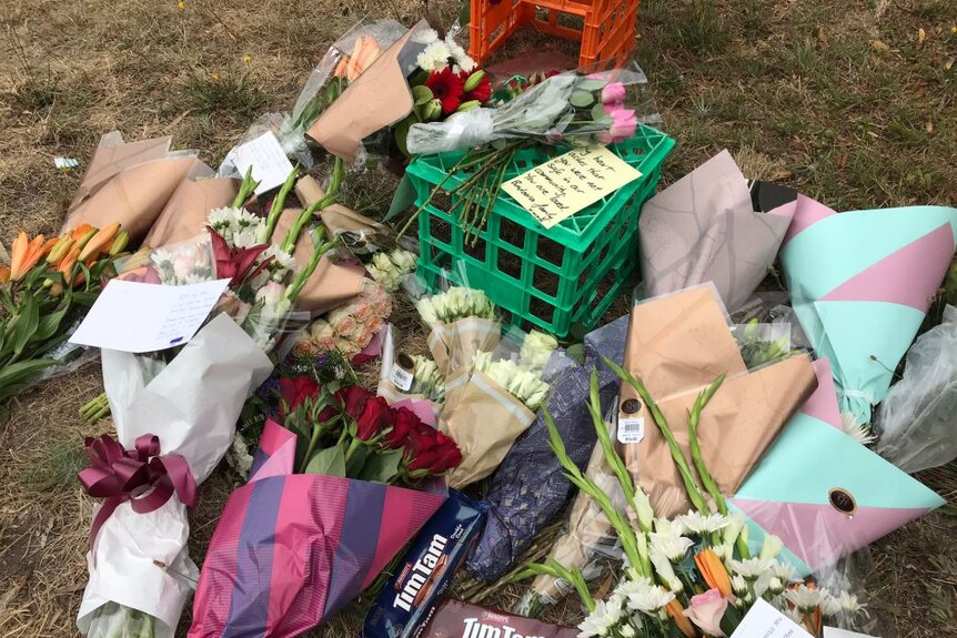 Bunches of flowers, cards and chocolate biscuit packets are laid out on a patch of grass.
