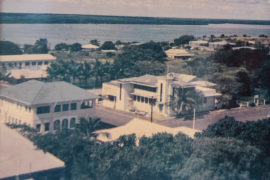 A faded photo, taken from a height, showing two large white bank buildings.  There are palm trees and the harbor beyond.