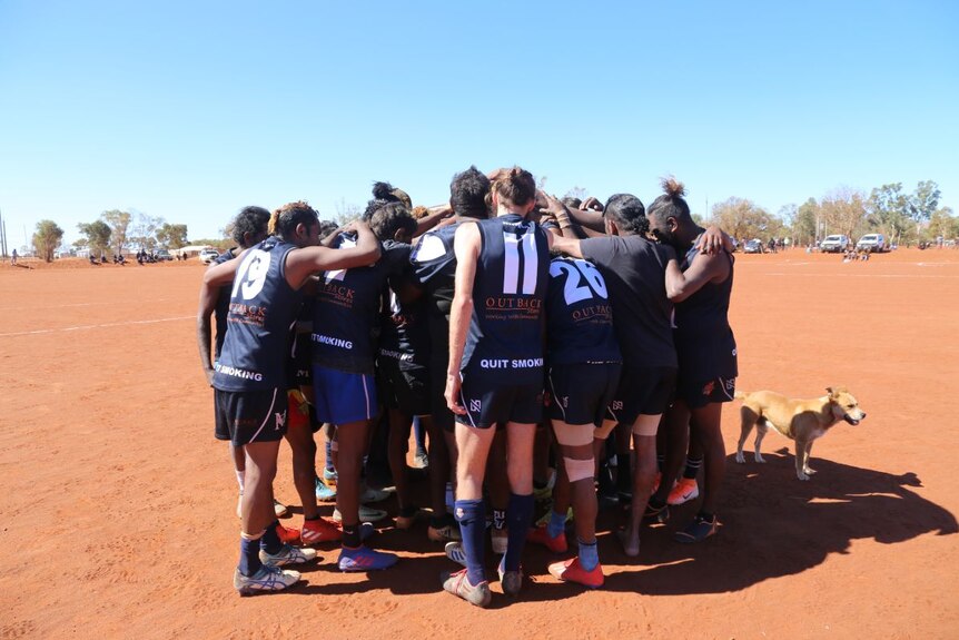 The Mimili Blues huddle on the oval for a prayer before they play.