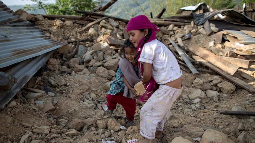 Two young girls move debris in Nepal from their collapsed home