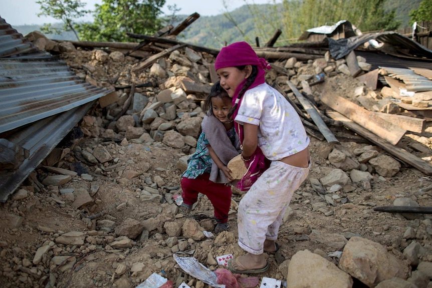 Two young girls move debris in Nepal from their collapsed home