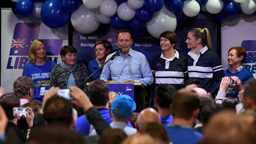 Tony Abbott speaks into a microphone surrounded by family members on stage.