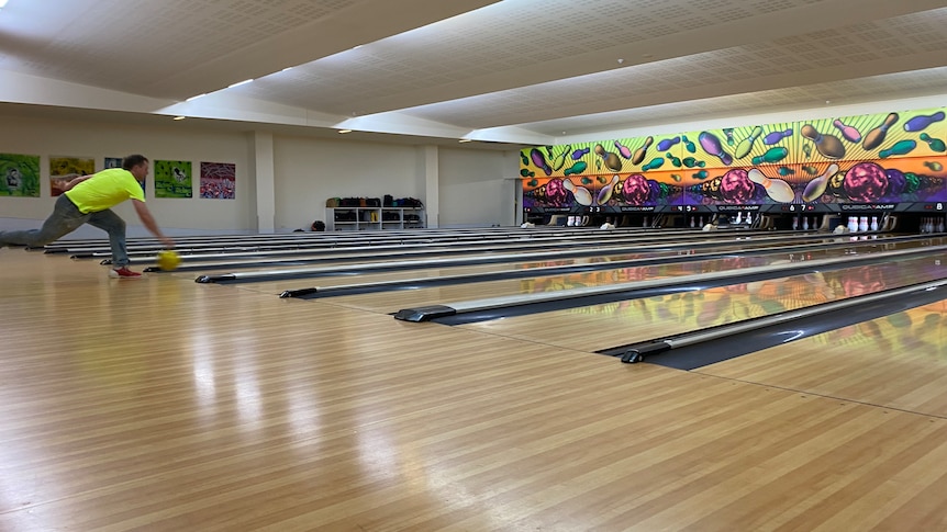 Man bowls a ball down a lane at a bowling alley.