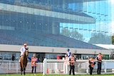 Riders and horses stand in front of a grandstand with no people in it