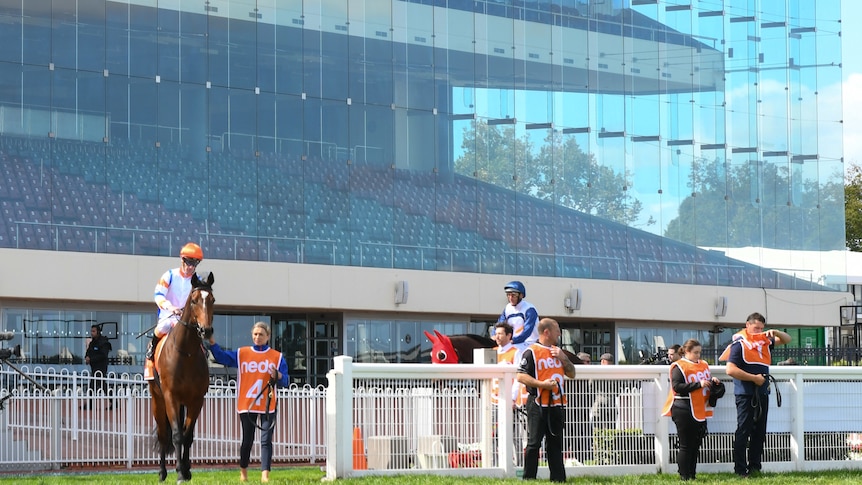 Riders and horses stand in front of a grandstand with no people in it