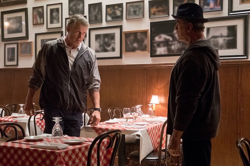 Colour still of Dolph Lundgren and Sylvester Stallone standing in restaurant in 2018 film Creed II.