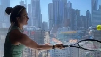 A woman in a green singlet hits a tennis ball against a floor to ceiling hotel window in Melbourne.