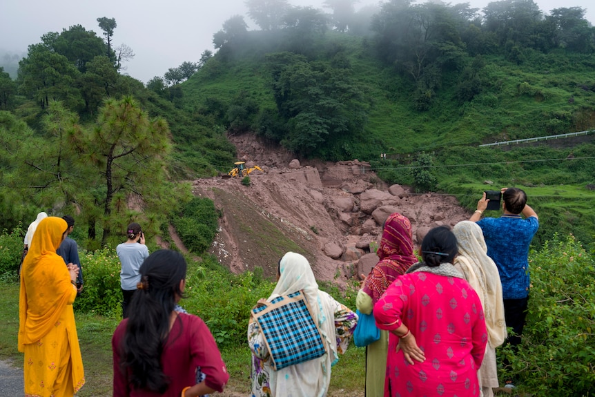 People looking and taking photos at the site of a landslide in a lush green landscape