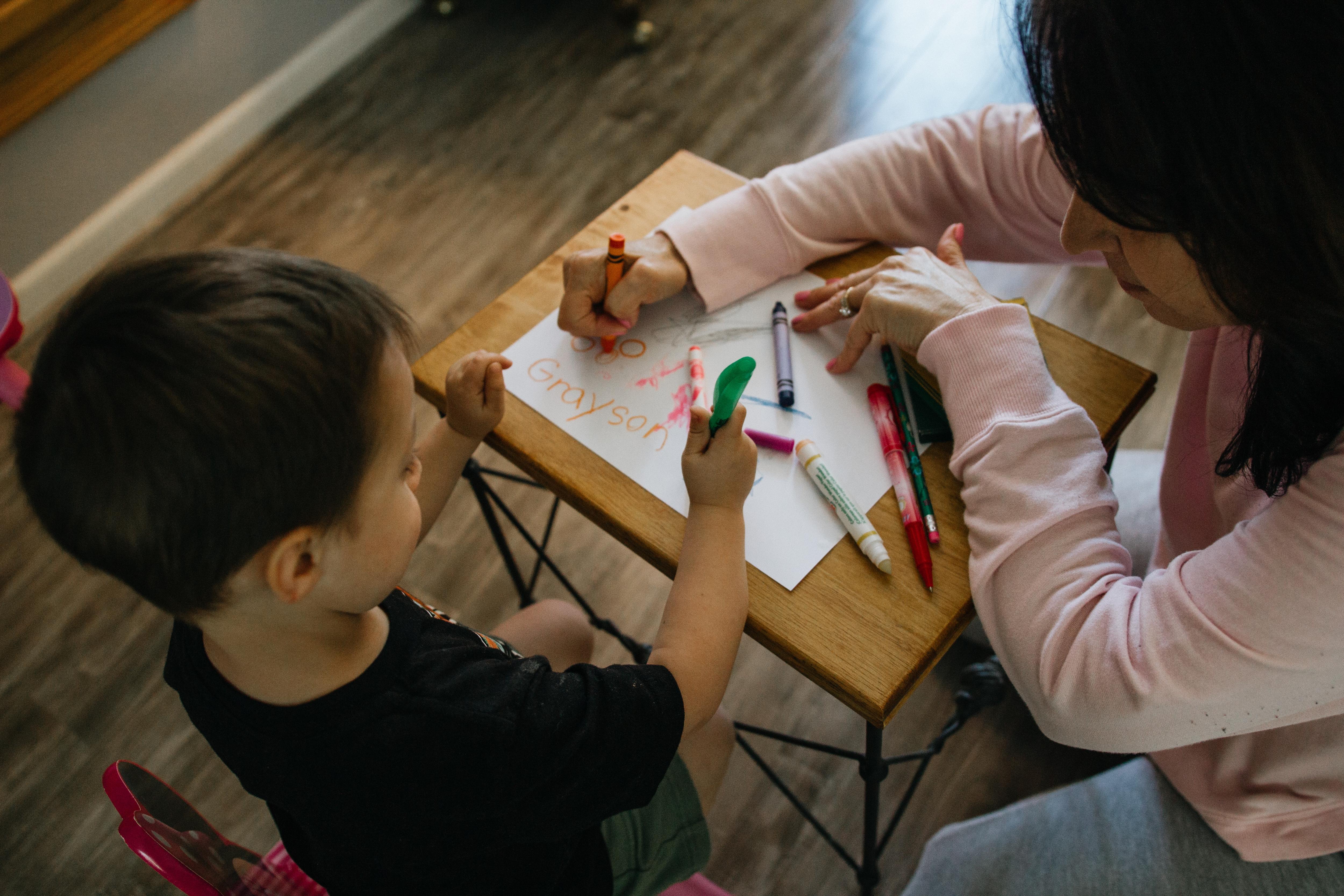 A mother plays with her kid, drawing at a table.