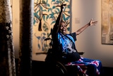 Artist Dhambit Munungurr sits in her wheelchair, smiling, with her hands raised in celebration.