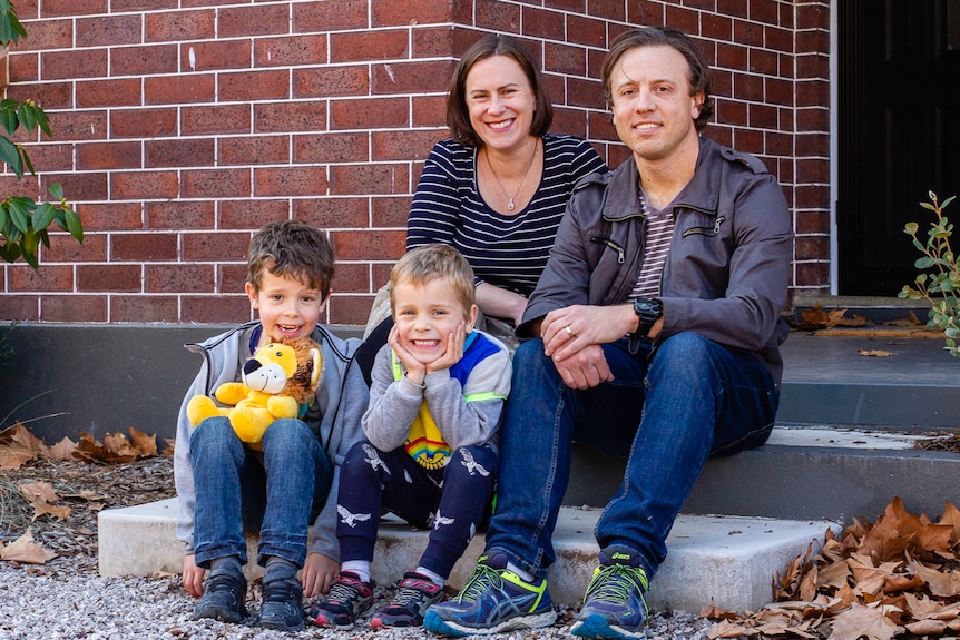 A family of two parents and two children sitting on the steps of a brick house, after their tree change to Orange in country NSW