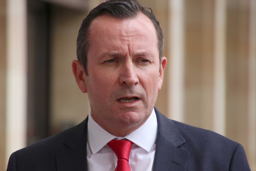 A tight head and shoulders shot of WA Premier Mark McGowan speaking wearing a black suit, white shirt and red tie.