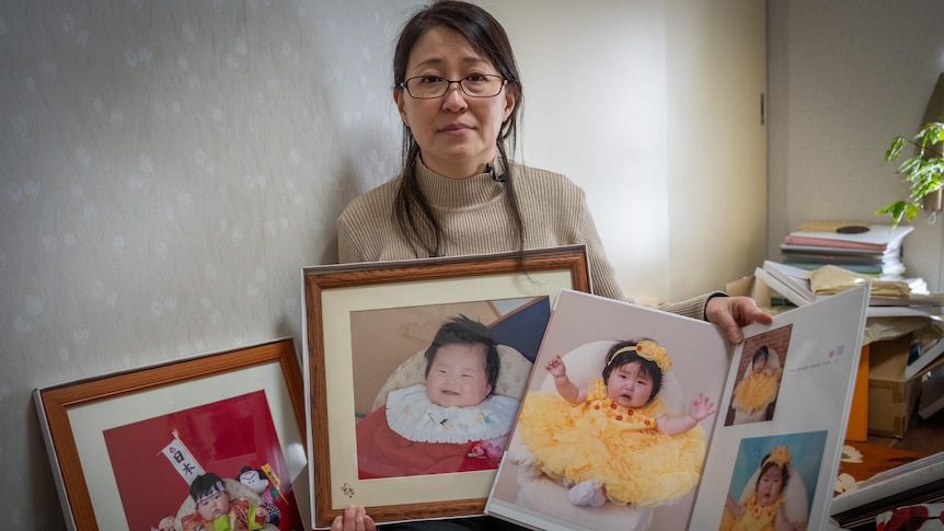 A woman holding photos of her three children.